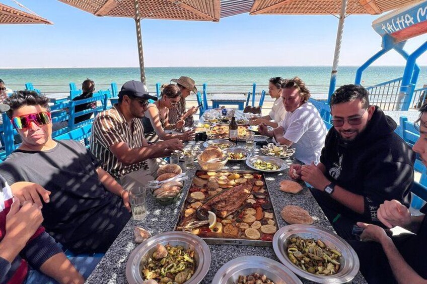 A group of people dining at a table on a boat with a view of the sea. 1