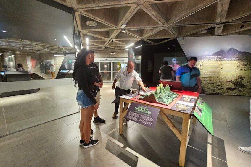 An indoor exhibit with a table displaying a model of a landscape and informational posters. 3