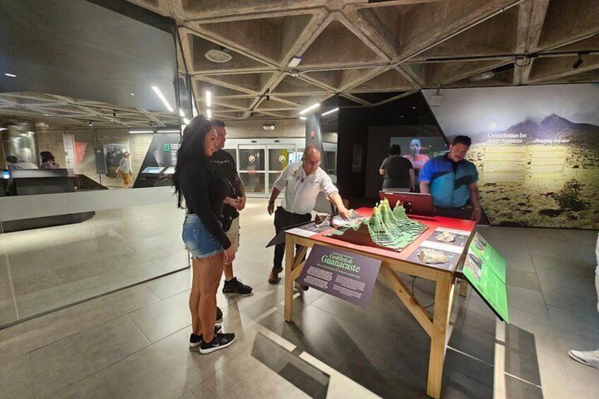 An indoor exhibition with a display table, informational signs, and a large wall mural. 3