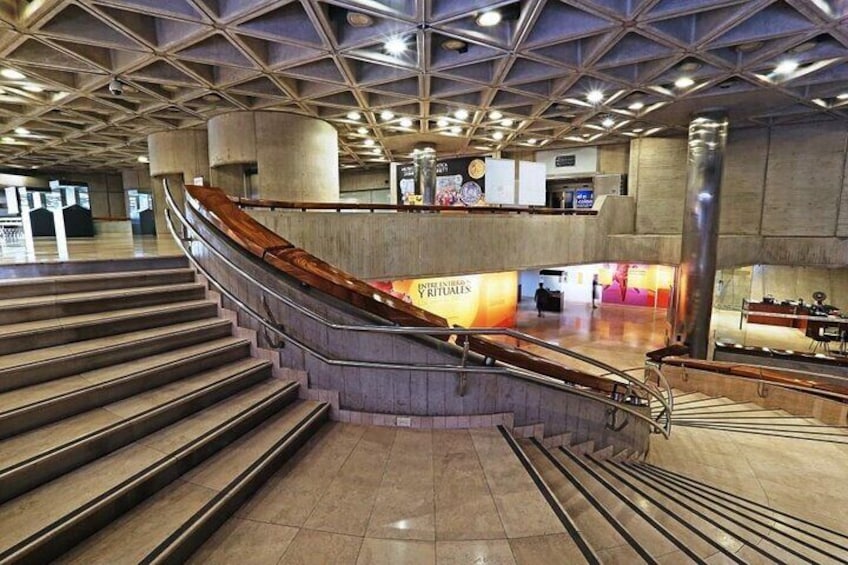 A modern indoor space with a curved staircase, a central pillar, and a counter with a sign. 4