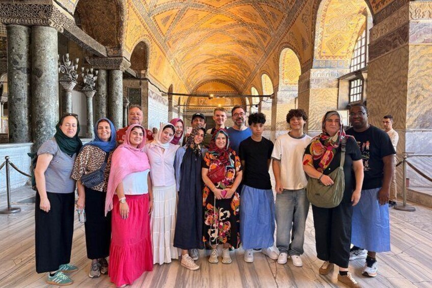 Un grupo de personas de pie frente a un edificio histórico con arcos y columnas ornamentales. 2