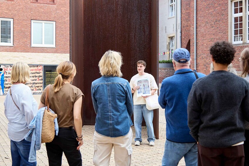 A group of people standing in an outdoor area with brick buildings and a large wooden door in the background. 5