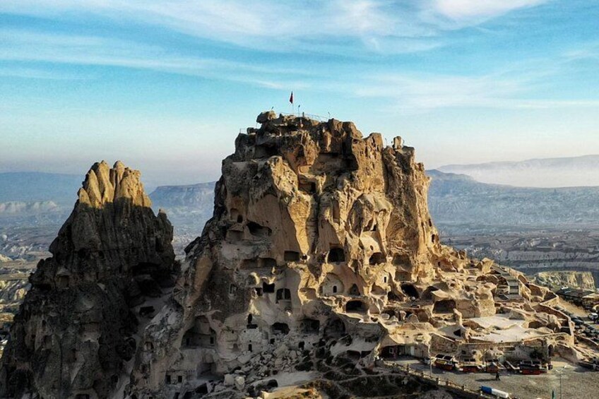 A rocky mountain with ancient cave dwellings and a flag on top. 5