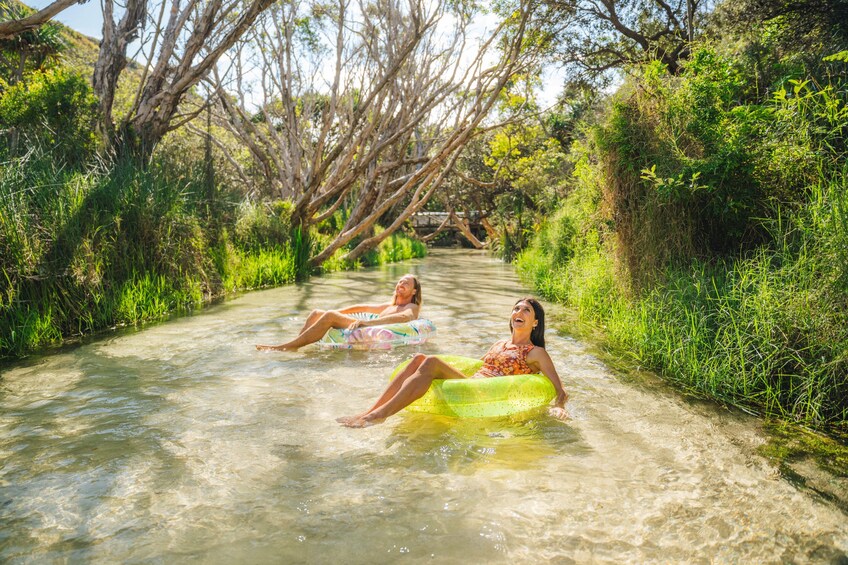 Two people floating on a river in a natural setting with trees and greenery. 3