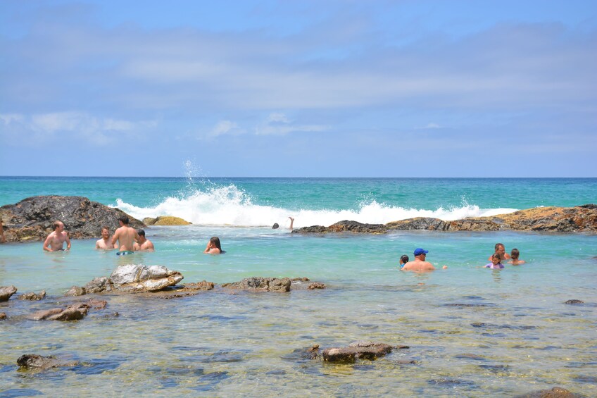 People swimming in a rocky coastal area with clear turquoise water. 1