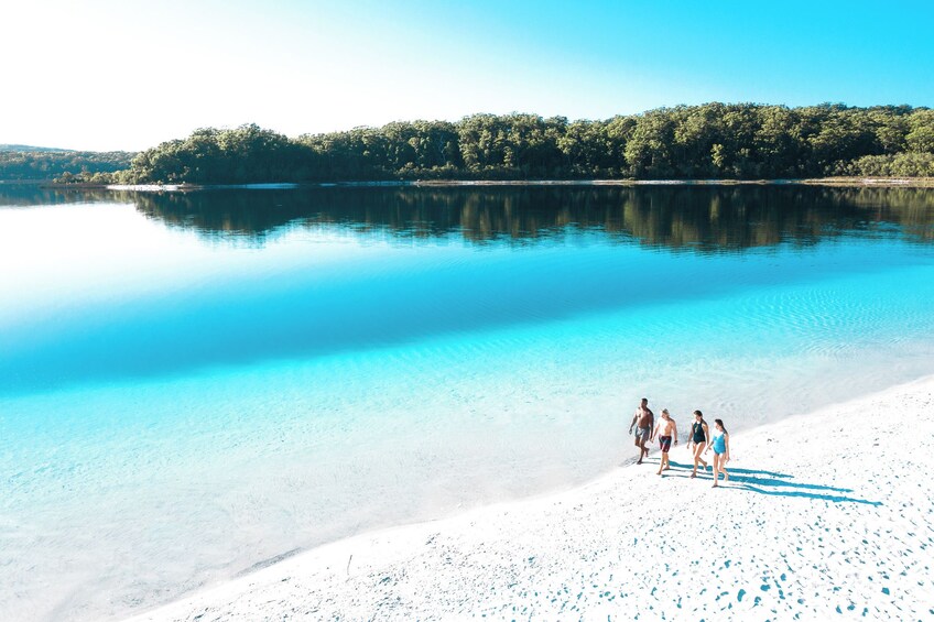 A beach with clear blue water and a group of people walking on the shore. 2