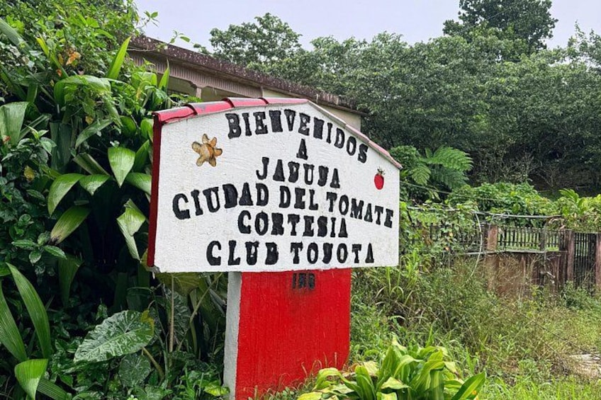 Welkomstbord voor Ciudad del Tomate, Club Toyota, omringd door weelderige begroeiing. 2