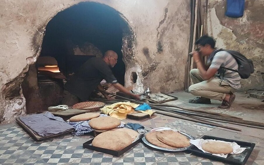 Two people working inside a cave-like structure with baked goods on the floor. 2