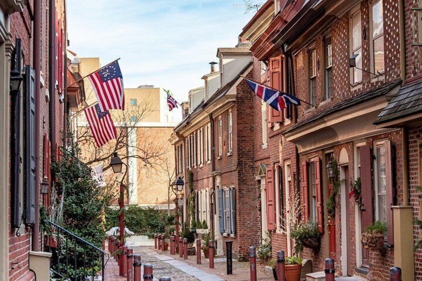 A narrow street lined with brick buildings, American flags, and a Union Jack flag. 2