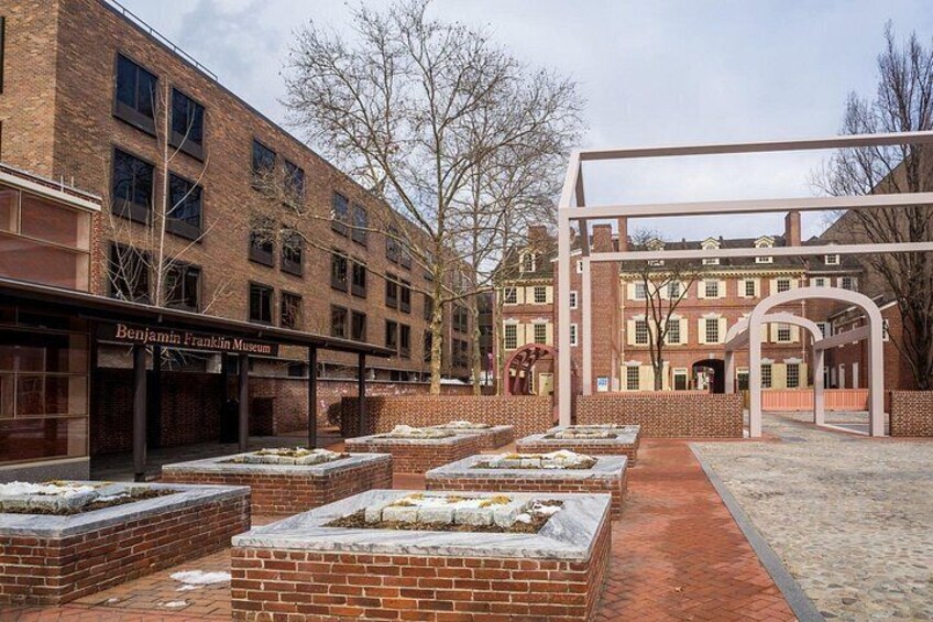 A courtyard with brick planters, a Benjamin Franklin Museum, and a historic building. 4