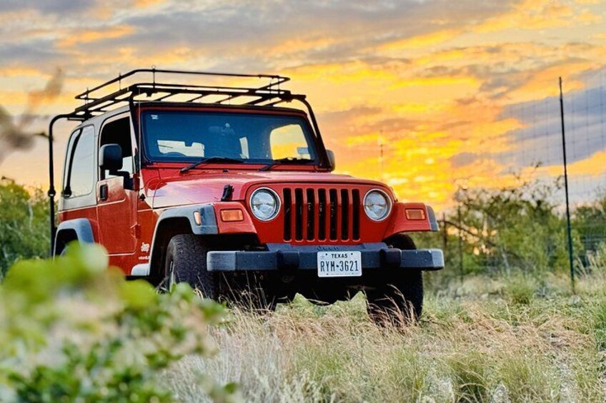 A red off-road vehicle parked in a grassy field with a sunset in the background. 2