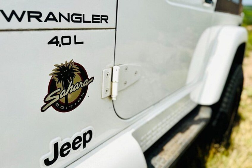 A white Jeep Wrangler 4.0L with a Sahara Edition logo and the word 'Jeep' on the side. 3