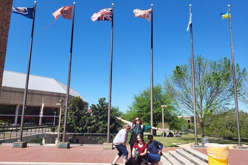 A group of people standing in front of a building with multiple flags on flagpoles. 3
