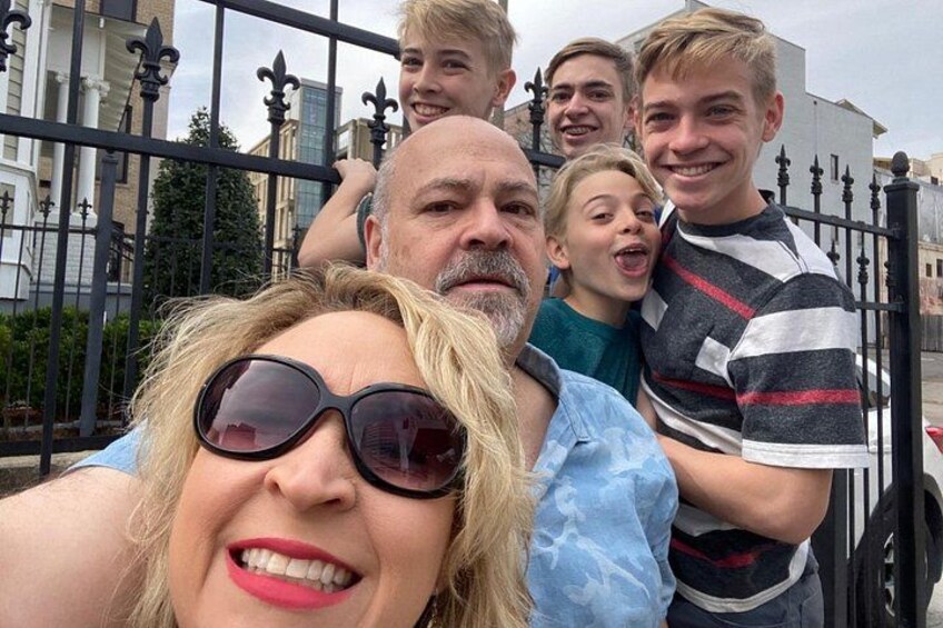 A group of people taking a selfie in front of a black wrought iron fence with buildings in the background. 2