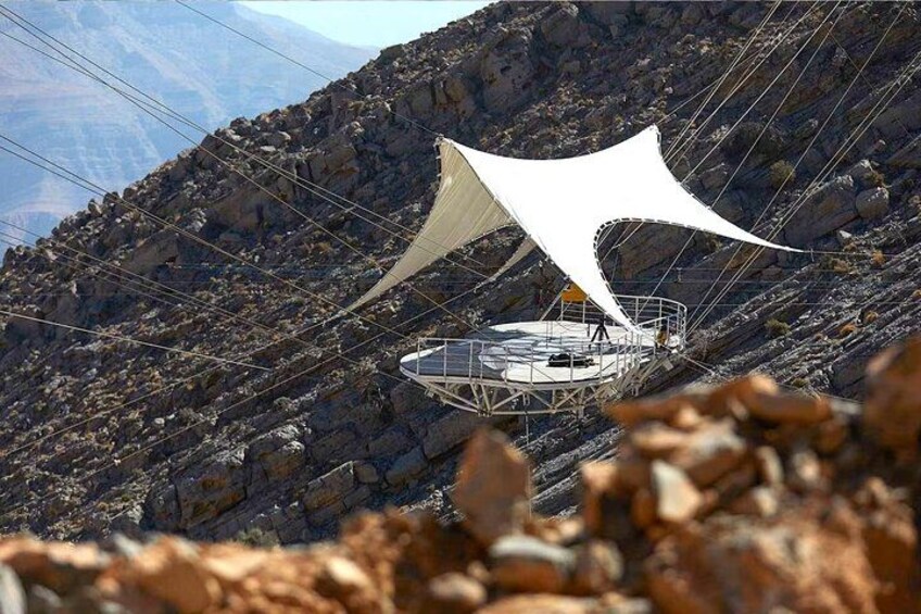 Een witte luifelconstructie op een rotsachtige berg met een rond platform. 4
