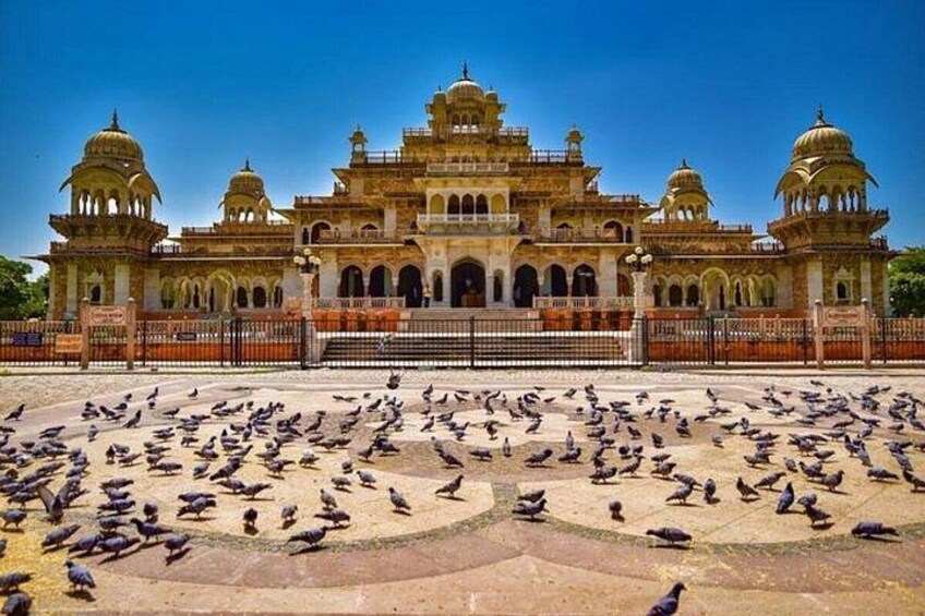 A historic building with domes and arches, surrounded by a large number of pigeons. 4