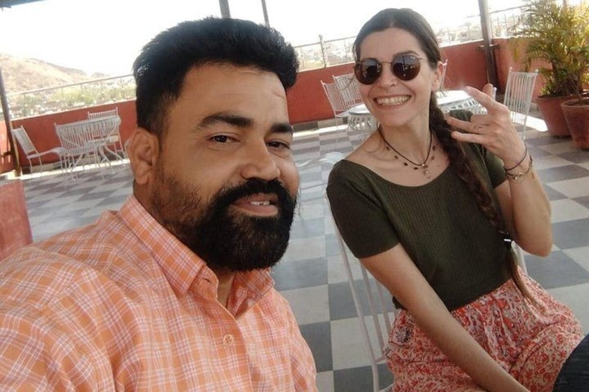 A man and a woman taking a selfie on a rooftop terrace with chairs and potted plants in the background. 3