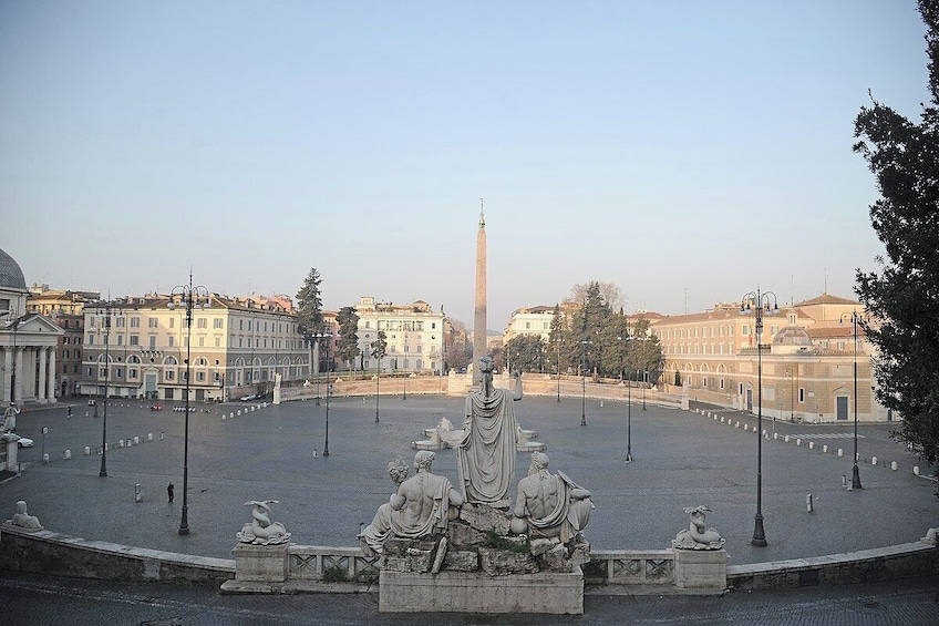 A plaza with a central monument and statues, surrounded by buildings. 3