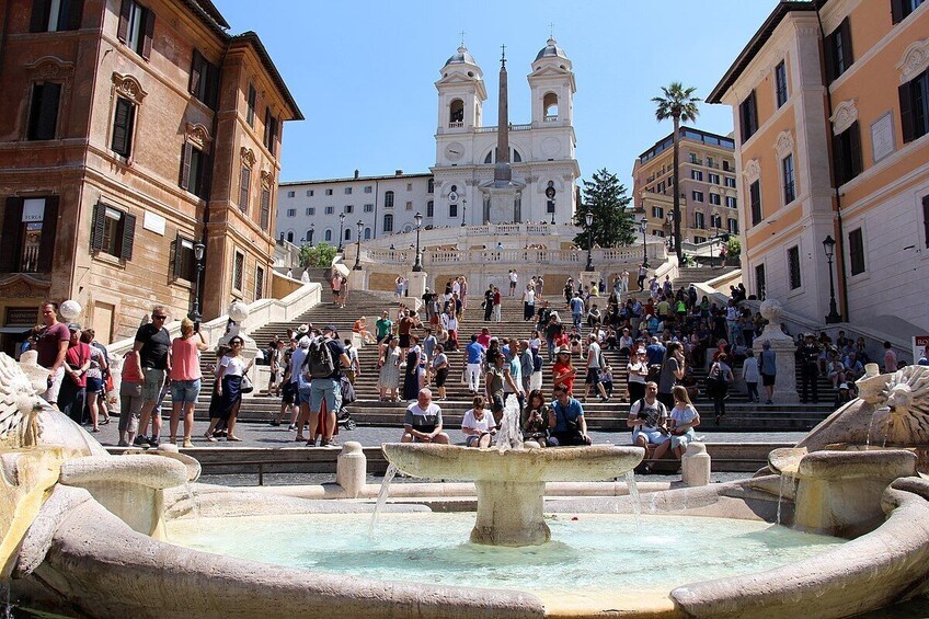 A crowded square with a large fountain and a prominent church in the background. 4