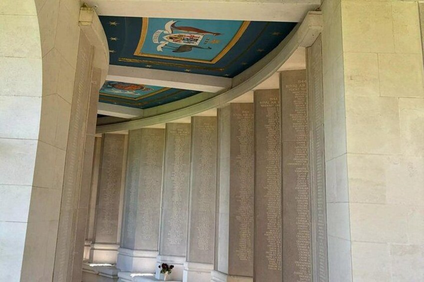 A corridor with a curved ceiling, columns with engraved text, and a floral arrangement. 4