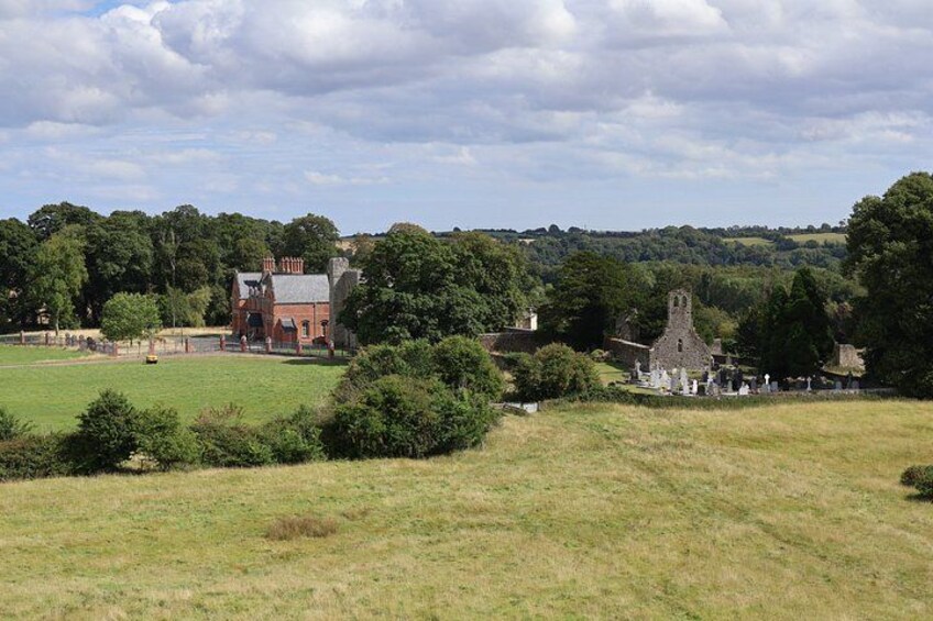 A rural landscape with a large field, a red brick building, and a church with a tower. 4