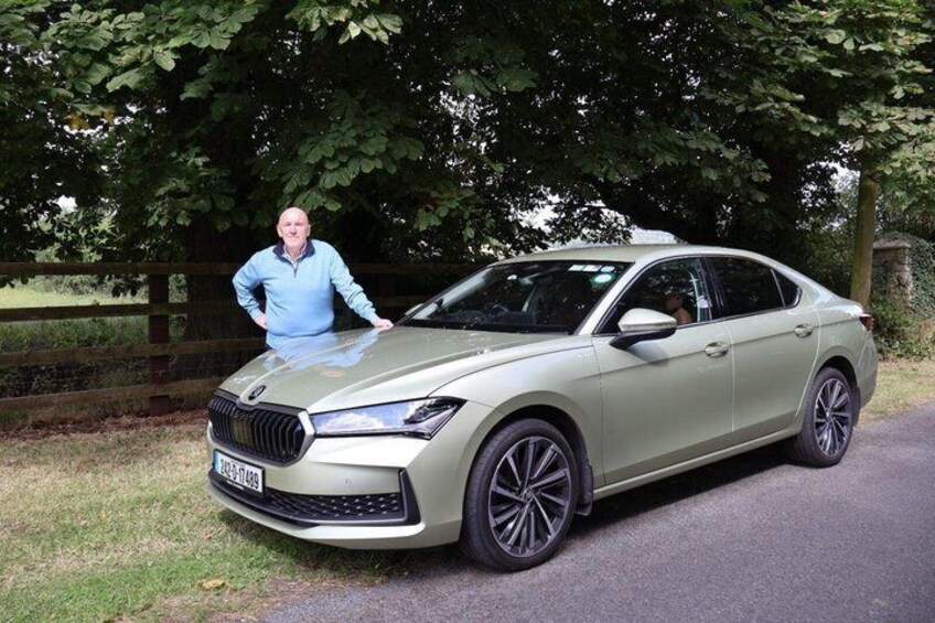 A beige BMW sedan parked on a paved road with a person leaning on the hood. 2