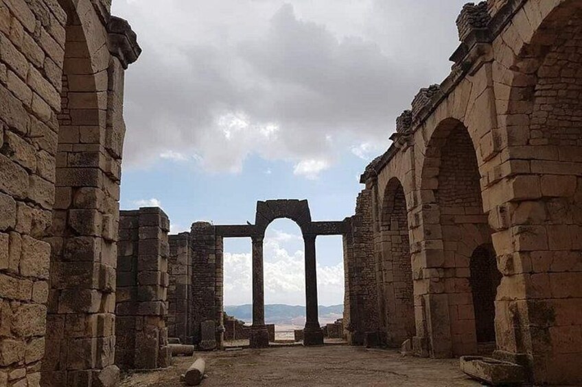 Ancient stone ruins with arches and columns, a clear sky, and distant mountains. 2