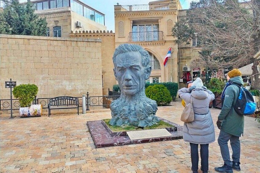 A bust sculpture in a courtyard with a bench, a flag, and a building in the background. 3