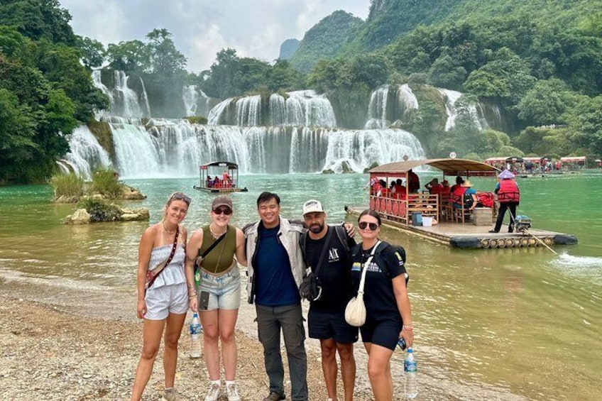 A group of people standing by a waterfall with a boat and a dock in the background. 3