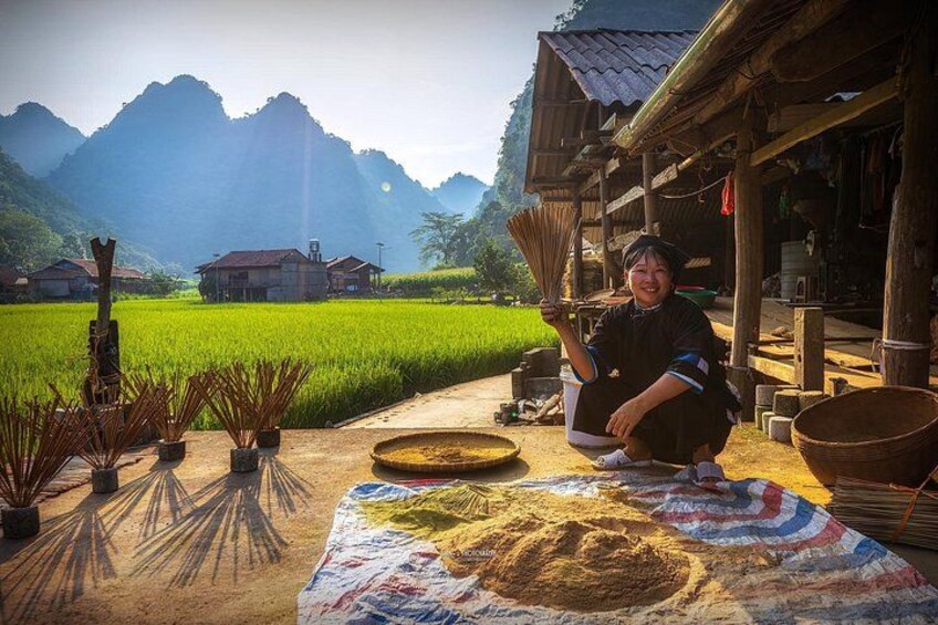 A person sitting on the ground with a table of rice and cooking utensils in a rural setting with mountains in the background. 2