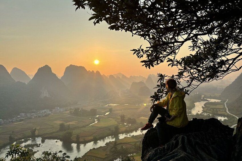 A person sitting on a rock overlooking a valley with mountains and a river. 3