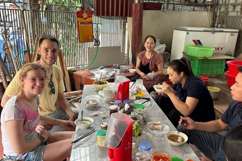 A group of people sitting at a table with food and drinks, in an outdoor setting with a metal fence and a refrigerator in the background. 4