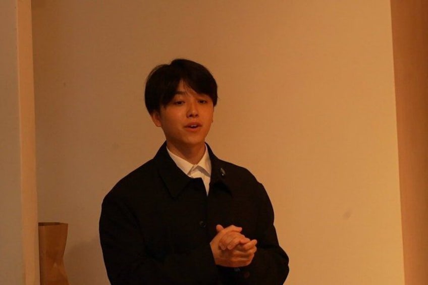 A person standing indoors, wearing a dark jacket and a white shirt. 4