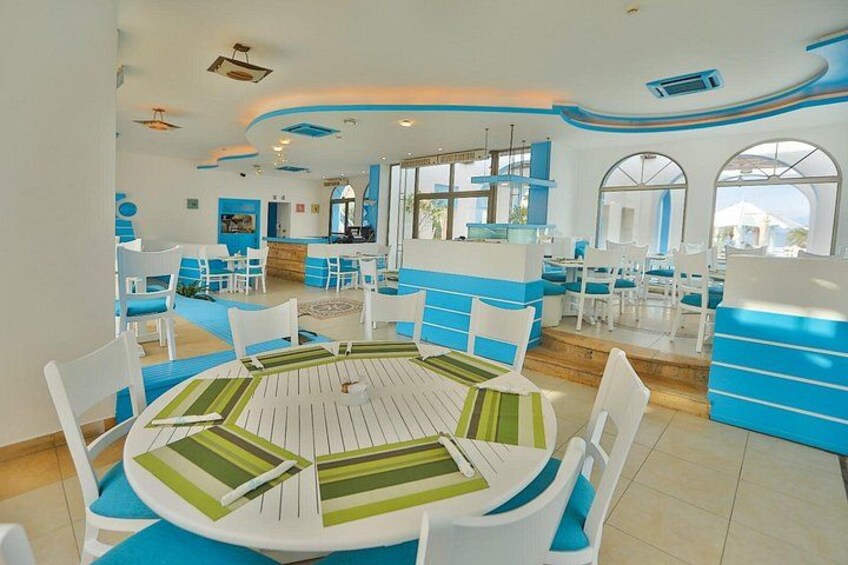 A modern dining area with white and blue furniture, a round table, and a kitchen in the background. 2