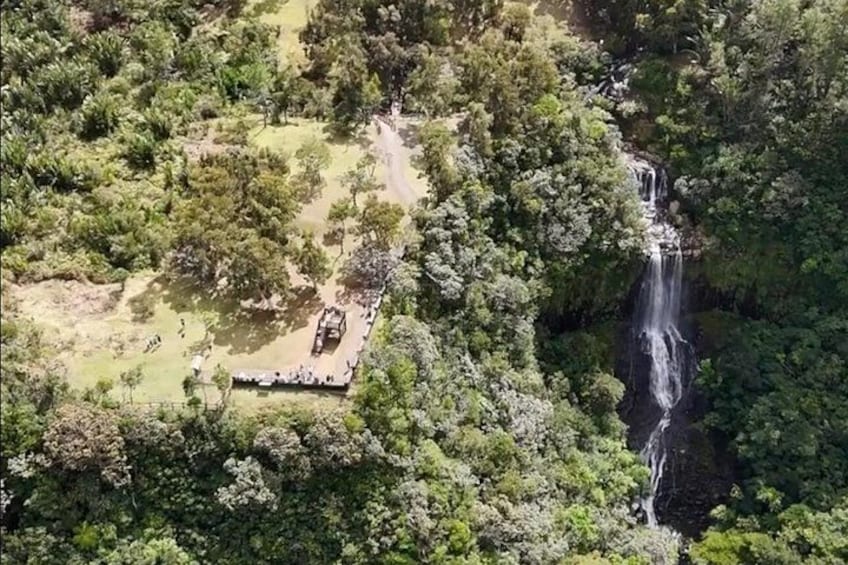 A waterfall, dense forest, and a paved area with a structure. 3