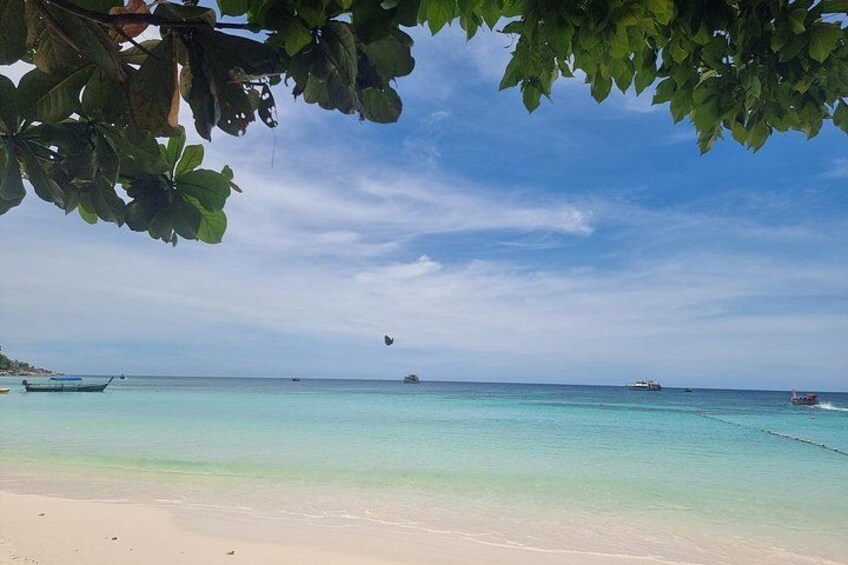 A beach with clear turquoise water, a boat on the left, and a distant ship. 5