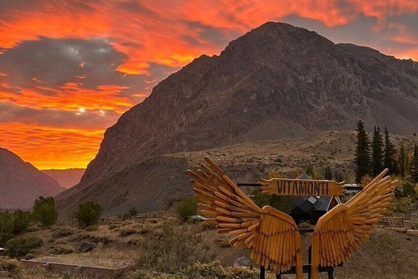 Cordillera con un atardecer, un letrero que dice 'VITAMONTI' y una estructura con alas amarillas. 2