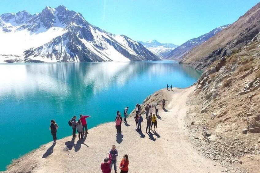 A group of people on a mountain path with a lake and snow-capped mountains in the background. 3