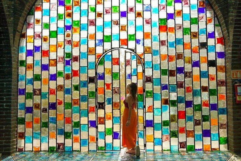 A person in orange robes standing in front of a colorful mosaic wall. 5