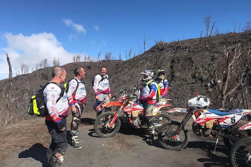 A group of people on a dirt road with dirt bikes, a hilly landscape, and leafless trees. 2