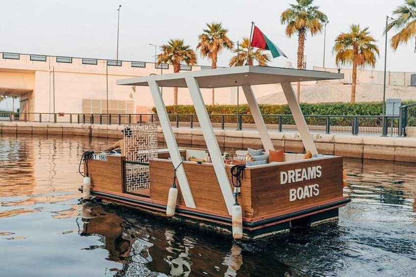 A wooden boat with a canopy and a flag, floating on water with palm trees and a building in the background. 3