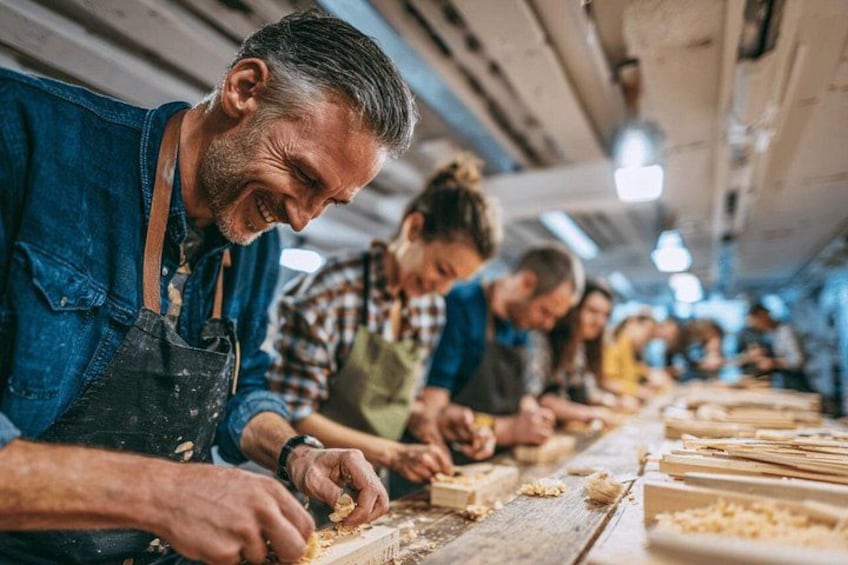 Menschen arbeiten an einem Tisch mit Holz, vermutlich in einer Werkstatt oder Schreinerei. 1