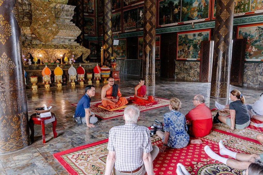 Een groep mensen in een tempel, met monniken, gebedsraden en traditionele decoratie. 2