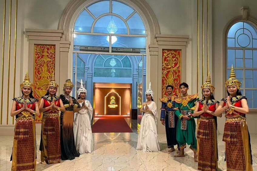 Un groupe de personnes vêtues de costumes traditionnels se tient dans un grand hall orné d’un lustre et d’un tapis rouge. 2
