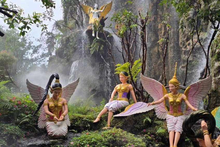 A group of statues in a forested area with a waterfall in the background. 5