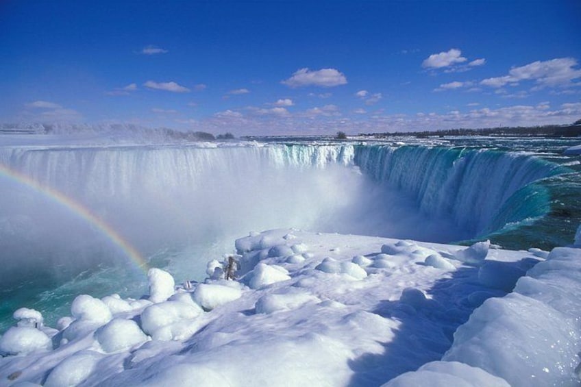 A waterfall with a rainbow, surrounded by snow and ice. 1