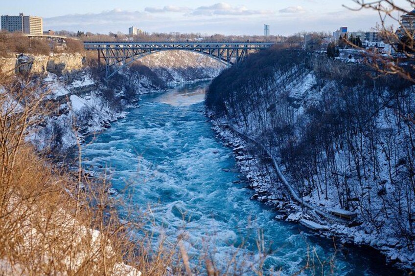 A river with a bridge, snow-covered banks, and buildings in the background. 4