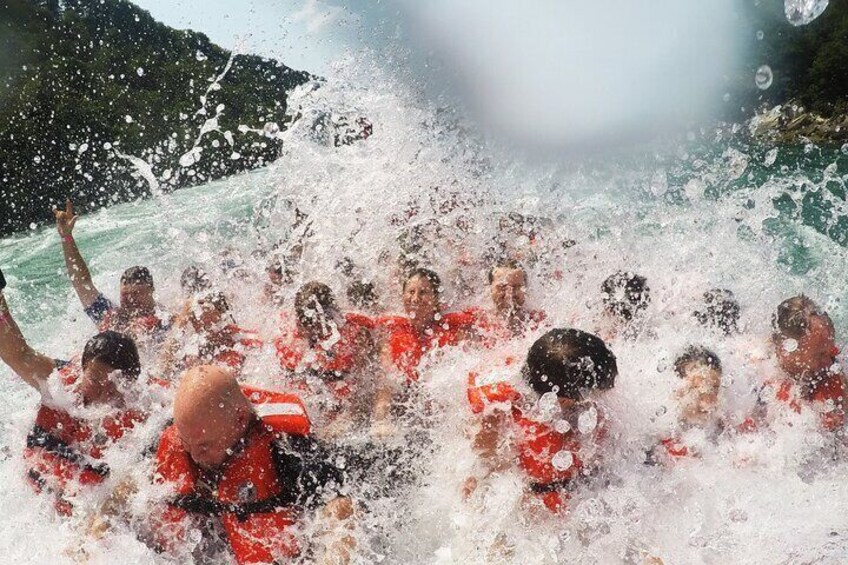 A group of people in red life jackets in a body of water, likely a lake or sea, with a mountainous background. 2
