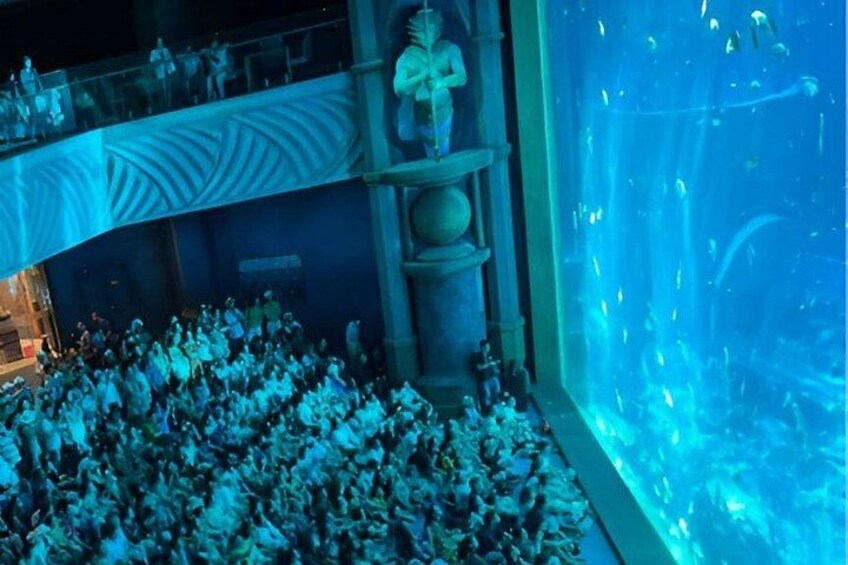 An aquarium with a large crowd of people, a statue, and an underwater viewing area. 5