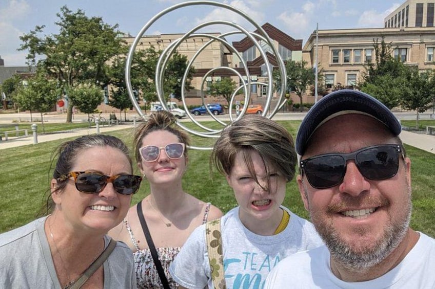A group of people posing in front of a sculpture with interlocking rings. 1
